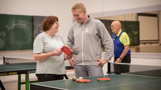 Tafeltennisster Josée en sportregisseur Roel van de Sande die samen naar het Kies je Sport 55+ boekje kijken, klik voor een vergroting
