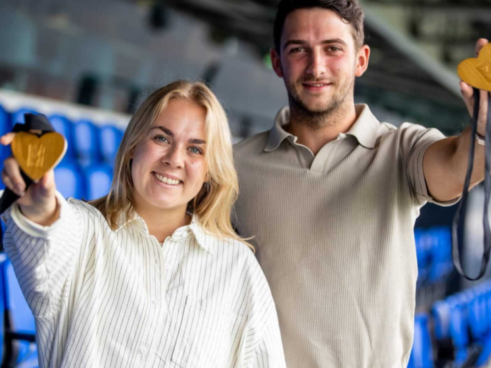 En jonge vrouw en man houden twee gouden medailles omhoog.